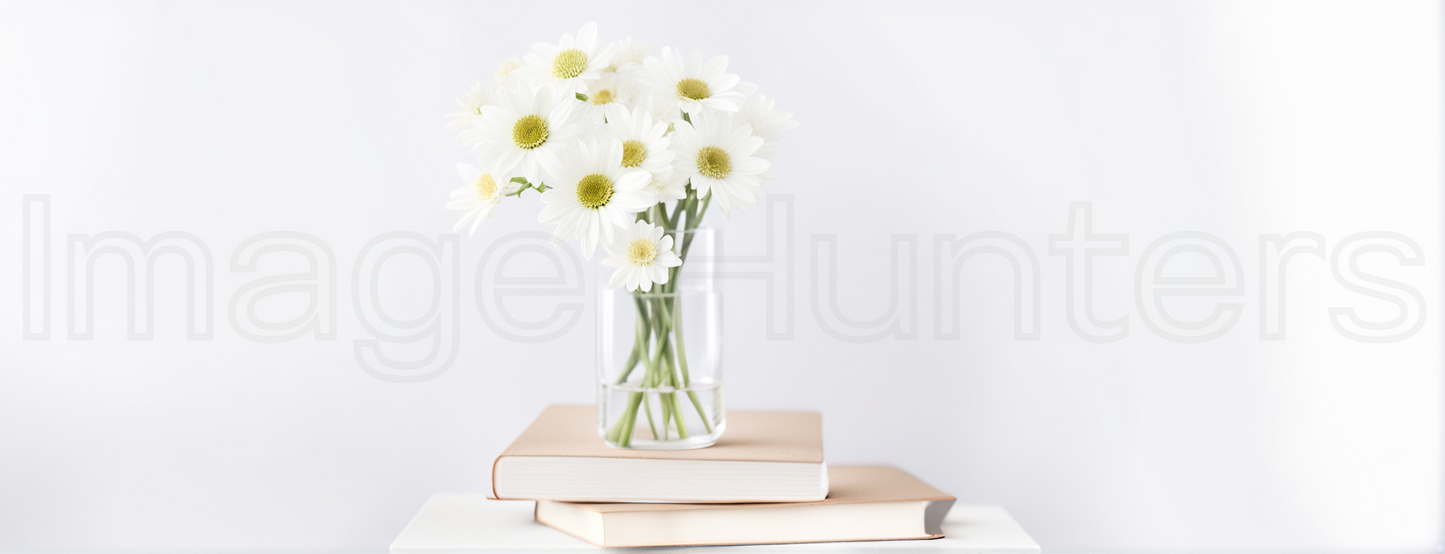 White flowers in transparent vase placed atop stack of books against white background